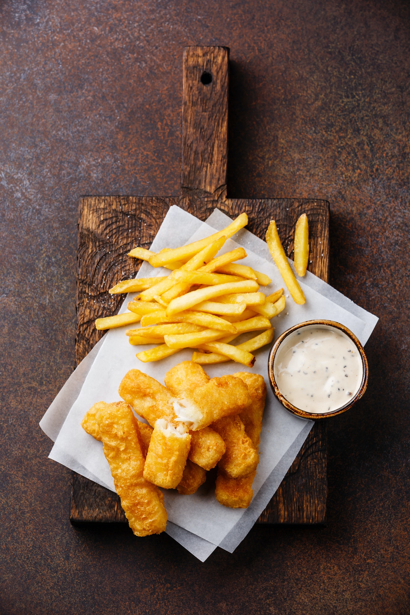 Fish fingers and Chips british fast food with tartar sauce on dark background
